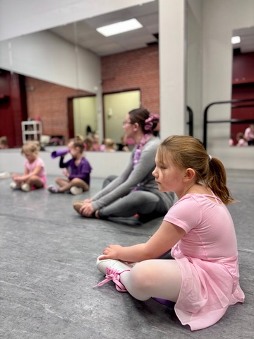 Young children in a ballet class sitting on the floor during a lesson at Ark Dance Academy